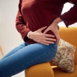 Image of a woman with her hands gripping her hip in pain.